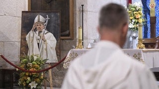 Ein Bild des verstorbenen Papstes Franziskus in einer Kirche | Tod von Papst Franziskus: Was jetzt im Vatikan passiert