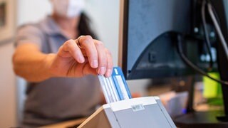Die Hausarztpraxen in RLP sind überlastet - eine Medizinische Fachangestellte schiebt in einer Hausarztpraxis die Versichertenkarte der Krankenkasse eines Patienten in das Lesegerät. 
