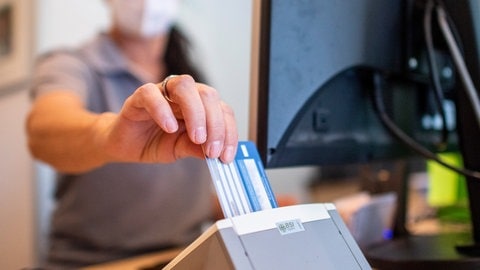 Die Hausarztpraxen in RLP sind überlastet - eine Medizinische Fachangestellte schiebt in einer Hausarztpraxis die Versichertenkarte der Krankenkasse eines Patienten in das Lesegerät. 