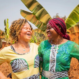 Zwei junge afrikanische Frauen, eine Frau hat Albinismus, stehen im Freien und lachen sich an: Menschen mit Albinismus verfolgt in schwarzafrikanischen Ländern wie Sambia tiefsitzender Aberglaube; sie sind von Geburt an stigmatisiert. Die Diskriminierung wurzelt in altem Aberglauben und ist schwer auszurotten. Doch die betroffenen Menschen wehren sich gegen das Stigma.