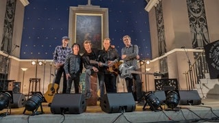 "Die Toten Hosen" stehen in einer Kirche gemeinsam vor dem Altar. Sie sind umgeben von Scheinwerfern, Mikrofonen und ihren Instrumenten.