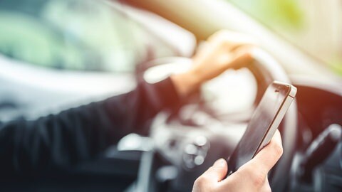 Mann hält Handy beim Fahren in der Hand