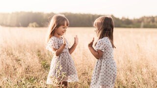 Zwei kleine Mädchen auf einer Wiese: Die Fingerabdrücke von eineiigen Zwillingen sind nicht identisch! Die Handlinien und auch die Fingerabdrücke sind zwar oft ähnlich, aber nie identisch. 