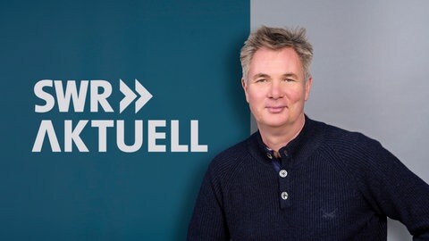 Gerald Pinkenburg steht vor dem Logo von SWR Aktuell.