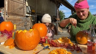 Eine Frau und ein Kind schnitzen bei Bauer Heini auf dem Erlebnisbauernhof Kürbisse 
