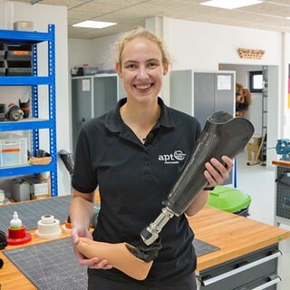 Junge Frau mit Zopf hält eine Prothese in der Hand.