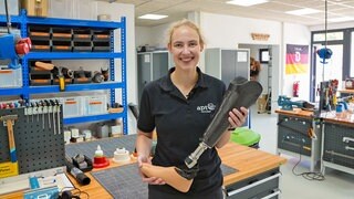 Junge Frau mit Zopf hält eine Prothese in der Hand.
