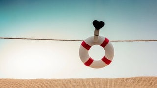 An einer Schnur befestigter Rettungsring mit schwarzem Herzsymbol: Mehr als 9.000 Menschen nehmen sich jedes Jahr in Deutschland das Leben. Forscherinnen und Forscher haben wirksame Therapien, Apps und Beratungskonzepte für Betroffene und Angehörige mit Suizidgedanken entwickelt. Allerdings fehlt Geld, um die Hilfsangebote überall verfügbar zu machen. 