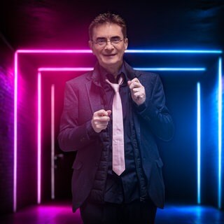 Kabarettist Mathias Richling lächelt vor einer leuchtenden Wand.
