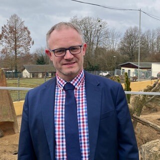 Oberbürgermeister Jan Einig steht am Gehege der Erdmännchen im Neuwieder Zoo