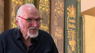 Mann ist vor alten Kochbüchern abgebildet
