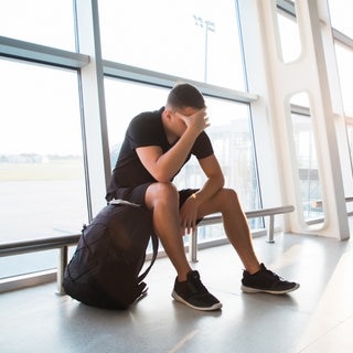 Ein trauriger junger Mann wartet am Flughafen auf seinen verspäteten Flug