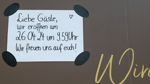 Lichtblick: Auf einem Schild steht: "Liebe Gäste, wir eröffnen am 26.04.24 um 9.59 Uhr. Wir freuen uns auf euch!"