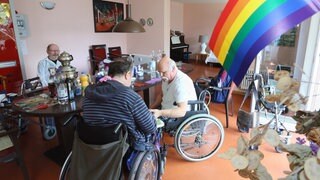Eine Regenbogen-Fahne schmückt 2015 den Gemeinschaftsraum der Wohngemeinschaft für homosexuelle Senioren in Berlin, die sich zum Mittagessen versammelt haben. Die WG im Berliner "Lebensort Vielfalt" ist eine Pflegeeinrichtungen für Homosexuelle, die sich in herkömmlichen Altenheimen vor Vorurteilen und Diskriminierung fürchten und zurückziehen. Mittlerweile, 2025, gibt es drei Wohnprojekt der Schwulenberatung in Berlin.