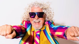 Älterer Mann mit grauem Haar und buntem Anzug lacht: Graue Haare sind eine optische Täuschung. Einzelne graue Haare gibt es gar nicht, denn sobald die Haarwurzel keine Pigmente mehr produziert, sind Haare farblos und erscheinen weiß. 