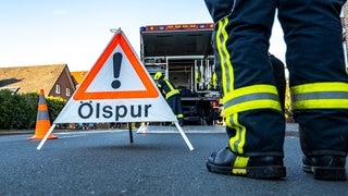 Ein Feuerwehrmann steht neben einem Warnschild mit der Aufschrift «Ölspur». 