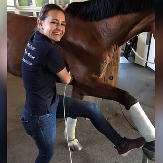 Tierärztin Sophie Kind arbeitet im Gestüt Marbach. Sie steht neben einem Pferd und streckt ein Bein aus.