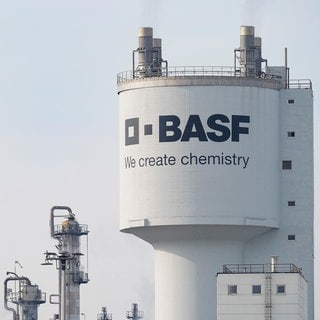 Ein Turm mit der Aufschrift "BASF" steht neben Schornsteinen auf dem Werksgelände des Chemiekonzerns BASF. Der Konzern muss sparen und will sich neu aufstellen.