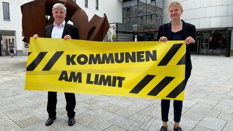 Landrat vom Kreis Tuttlingen und Bürgermeisterin der Stadt Trossingen halten ein gelben Banner mit schwarzer Schrift "Kommunen am Limit".