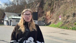 Adriana Dobihal steht vor ihrem Haus, was im Hintergrund leicht unscharf ist. Rechts des Hauses steht eine gelbe Sandsteinwand.