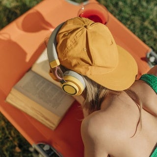 Person mit Kopfhörern auf einer Liege liest ein Buch