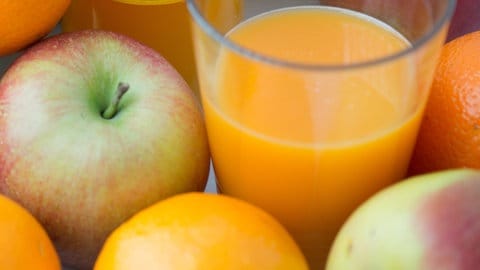 Ein Glas mit Fruchtsaft aus einer Flasche steht inmitten von Äpfeln und Orangen.