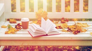 Parkbank mit Herbstlaub, Buch und Kaffeebecher