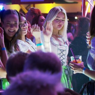 Viele Menschen in Dirndl und Leder feiern ausgelassen in einem Festzelt.