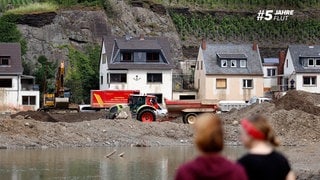 Zwei junge Menschen stehen im Mayschoss am Ahrufer und schauen auf die Zerstörung durch das verheerende Hochwasser im Ahrtal.