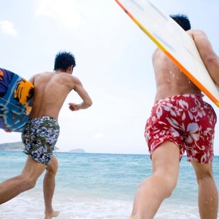 Zwei junge Männer in Badeshorts laufen mit Surfboards ins Wasser