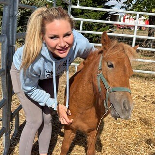 Madeleine „Maddy“ Morhardt steht mit einem Pferd in einer Kuppel. Sie lächelt in die Kamera.