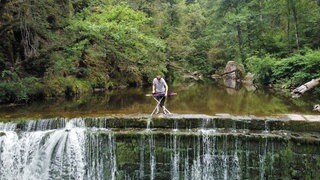 Extrembügler steht über einem Wasserfall und bügelt.