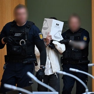 Ein Polizist führt Sulaiman A. für das Urteil in den Gerichtssaal des OLG Stuttgart-Stammheim.