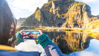 Handyaufnahme einer Bergkulisse auf den Lofoten: Reiseinfluencer berichten auf Instagram, TikTok und YouTube über ihre Trips. Sie zeigen paradiesische Strände, luxuriöse Hotels oder abgelegene Naturorte. Millionen Menschen lassen sich davon inspirieren.