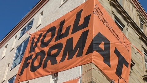 Orangene Banner mit Öffnungszeiten und Titel "Vollformat" zieren das Haus in der Johannesstraße 47b in Stuttgart