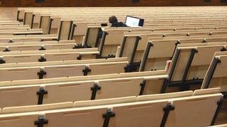 An einer Universität sitzt ein Student in einer Vorlesung im Auditorium.