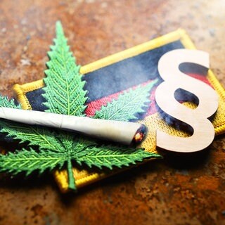 Cannabisblatt-Symbol, Joint, Paragrafenzeichen auf Deutschlandfahne: Das Cannabisgesetz wird evaluiert. Erste Ergebnisse zeigen: Mehr konsumiert wird nicht. Probleme bereiten die vielen Telemedizin-Plattformen, die die Verschreibungen sehr leicht machen.
