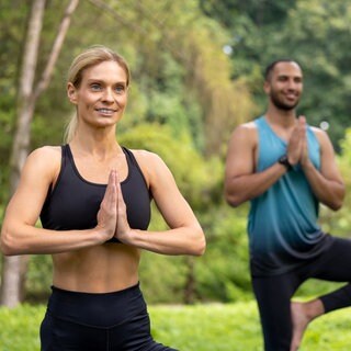 Eine Frau und ein Mann machen Yoga-Übungen in einem Park: Millionen Menschen machen Yoga, weil sie Körper und Seele gesund halten möchten. Aber Atmen, Meditation und Asanas können auch Kranken helfen, gesund zu werden. Das belegen Studien. 