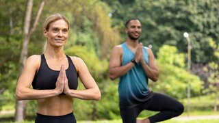 Eine Frau und ein Mann machen Yoga-Übungen in einem Park: Millionen Menschen machen Yoga, weil sie Körper und Seele gesund halten möchten. Aber Atmen, Meditation und Asanas können auch Kranken helfen, gesund zu werden. Das belegen Studien. 