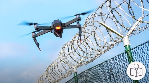 Das ist ein Beispiel·bild: Eine Drohne fliegt über einen Stachel·draht·zaun.  