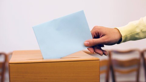 Eine Hand lässt einen Wahlzettel in die Urne fallen: Ehrenamtliche Bürgermeister für kleine Kommunen sind immer schwerer zu finden