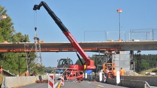 Ein Kran hebt ein Gerüst auf einer Autobahn an. 