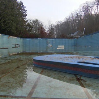 Ein leeres Schwimmbecken in dem trübes Wasser steht