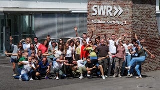Frauen und Männer stehen und knien vor dem Gebäude des SWR Studios Tübingen. 