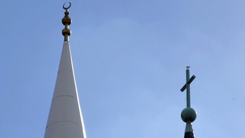 Eine Sichel auf dem Minarett einer Moschee und ein Kreuz auf einem Kirchturm. 