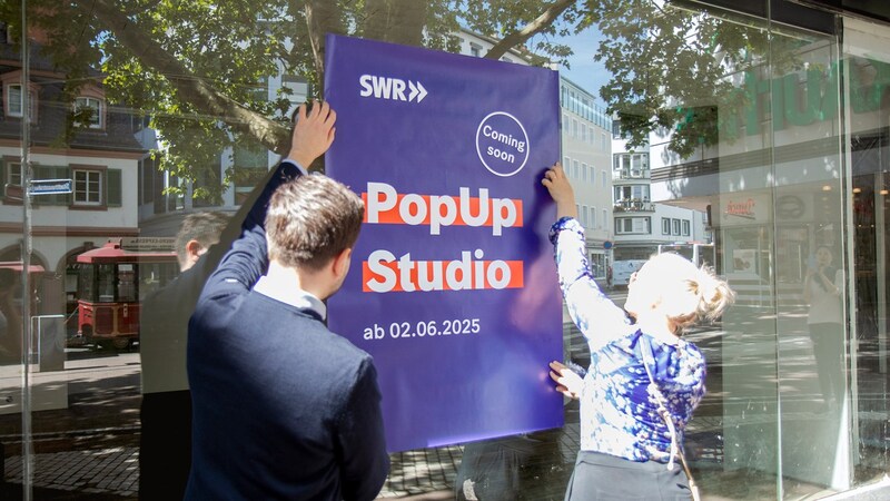 Annika Richter und Ibrahim Bilen vom SWR kleben Plakate am SWR PopUp Studio.