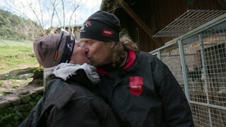 Carolin Engler und Michael Roupp stehen draußen vor einem Käfig und küssen sich.