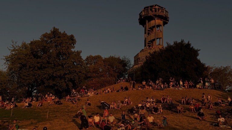 Am Seepark in Freiburg sitzen viele Menschen auf einer Anöhe auf der Wiese und schauen Richtung Sonne. Sie beobachten die Sonnenfinsternis.