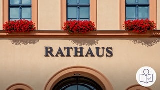 Ein Haus mit der Aufschrift Rathaus. An den Fenster sind Blumenkästen. Im Rathaus arbeitet der Bürger·meister. Er macht mit dem Gemeinde·rat die Poltik in der Kommune. Rechts das SWR Logo für Leichte Sprache.