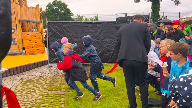 Kinder rennen durch eine geöffnete Absperrung auf einen Spielplatz. Der Unisport der Rheinland-Pfälzischen Technischen Universität Kaiserslautern-Landau (RPTU) hat auf dem Campus einen Abenteuerspielplatz eröffnet. Das Kitz-Land können Kinder mit einer Unisport-Karte besuchen.